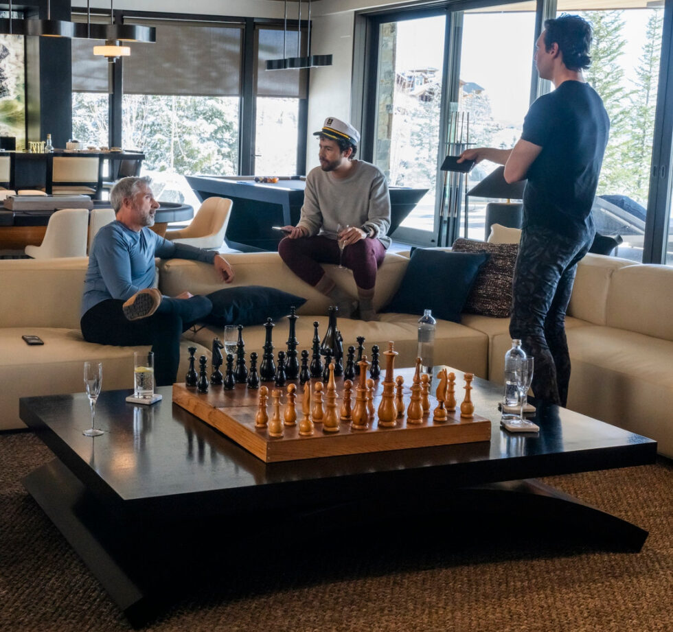 Photo of large chess board with three characters from Mountainhead talking around it, HBO publicity